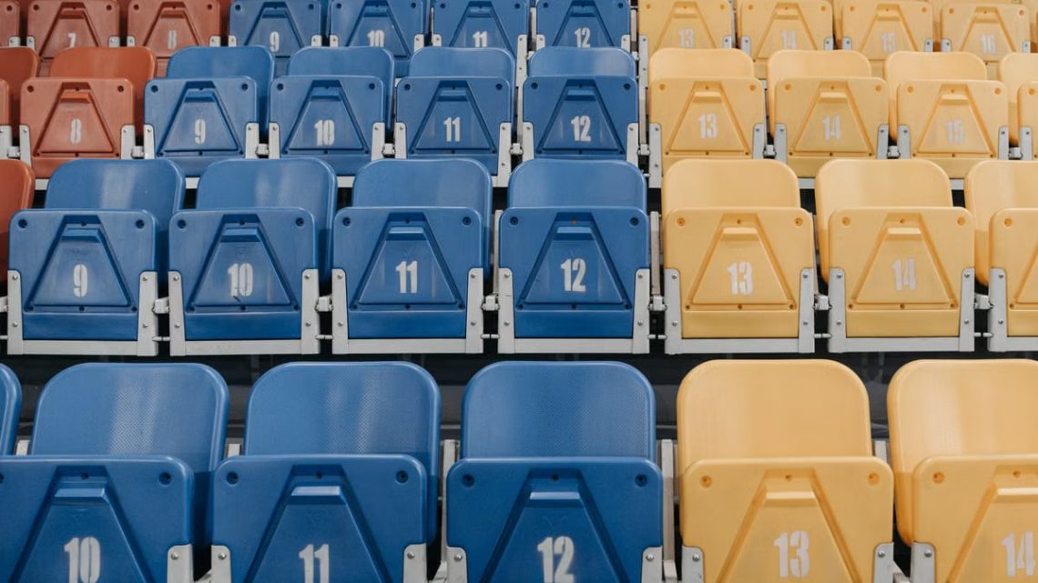 Uniform rows of red, blue, and yellow stadium seats with numbers visible.